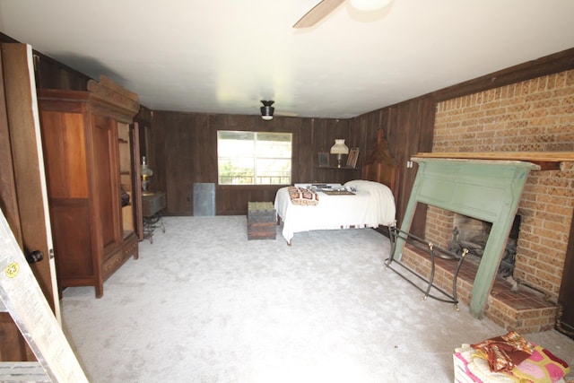 bedroom with a brick fireplace, ceiling fan, wooden walls, and light carpet