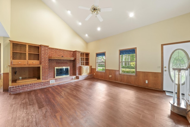 unfurnished living room featuring wood-type flooring, a fireplace, high vaulted ceiling, wooden walls, and ceiling fan