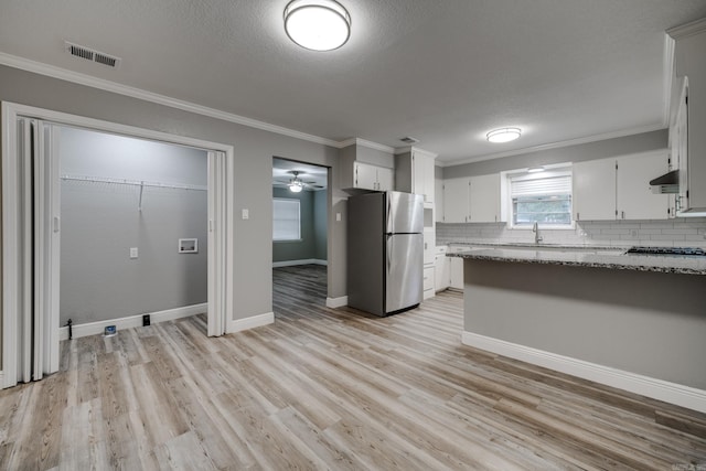 kitchen featuring white cabinetry, appliances with stainless steel finishes, light stone countertops, light wood-type flooring, and decorative backsplash