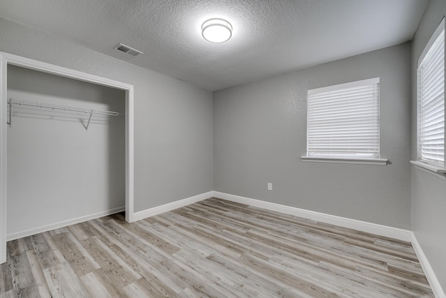 unfurnished bedroom with light hardwood / wood-style floors, a textured ceiling, and a closet