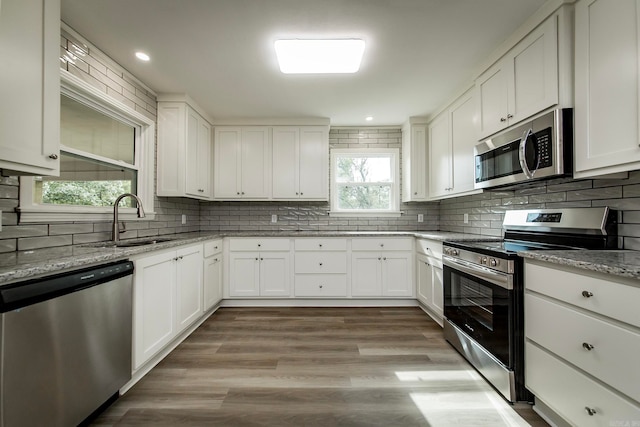 kitchen featuring stainless steel appliances, light stone counters, decorative backsplash, white cabinetry, and light wood-type flooring