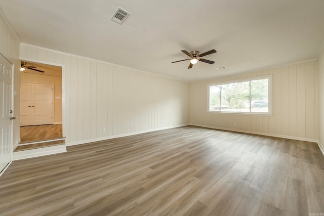 unfurnished room featuring ceiling fan, wood-type flooring, wood walls, and crown molding