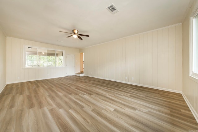 unfurnished room featuring wood walls, crown molding, ceiling fan, and light hardwood / wood-style flooring