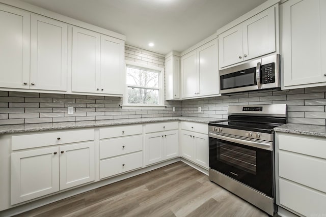 kitchen with light stone counters, backsplash, white cabinetry, light wood-type flooring, and appliances with stainless steel finishes