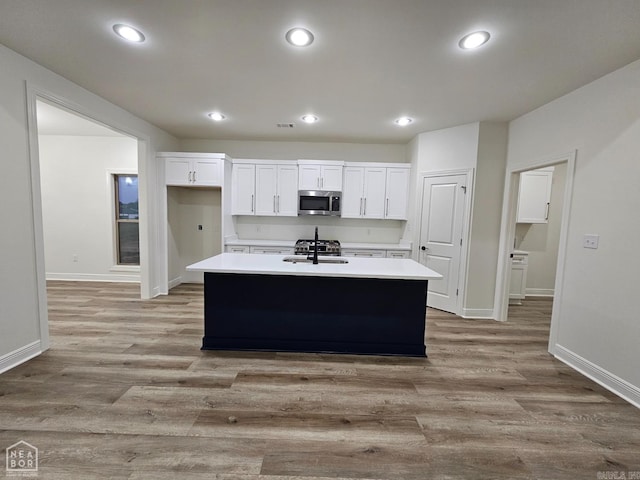 kitchen with a kitchen island with sink, light wood-type flooring, and white cabinets