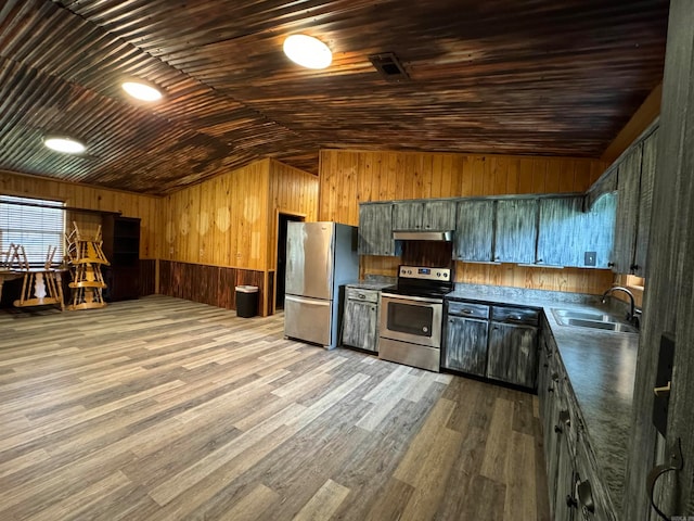 kitchen featuring wood walls, sink, appliances with stainless steel finishes, light hardwood / wood-style flooring, and vaulted ceiling