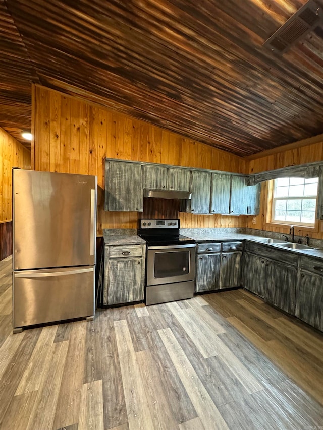 kitchen with vaulted ceiling, wood walls, sink, light wood-type flooring, and appliances with stainless steel finishes