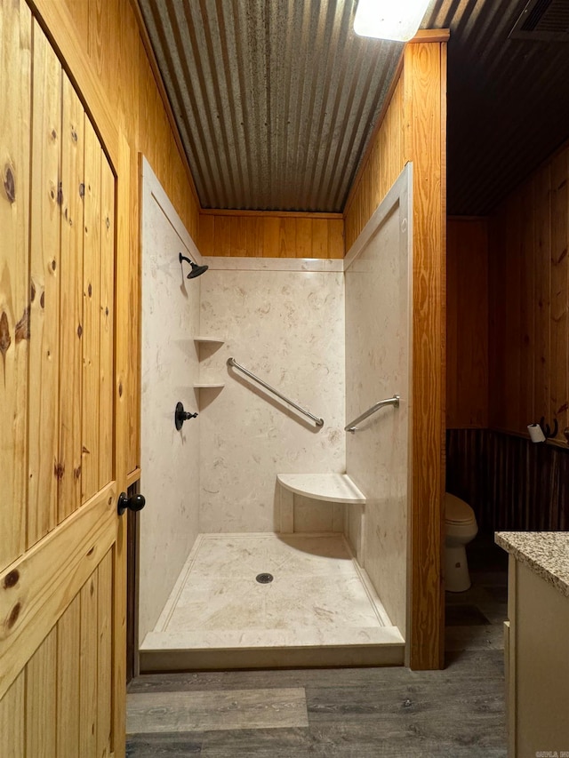 bathroom featuring hardwood / wood-style floors, wooden walls, a shower, and toilet