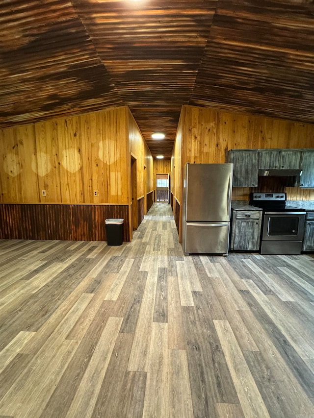 kitchen featuring hardwood / wood-style floors, stainless steel appliances, wood walls, and vaulted ceiling