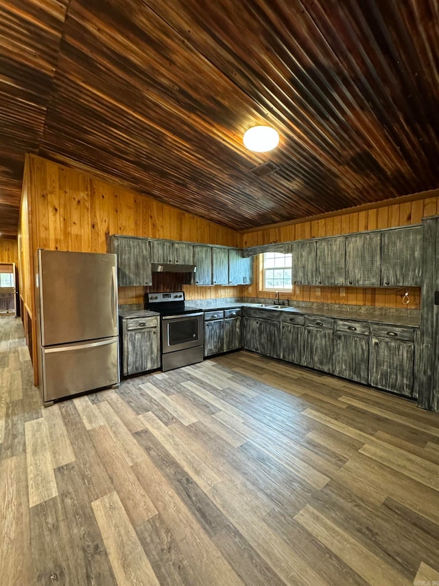 kitchen with stainless steel appliances, wooden walls, vaulted ceiling, wood ceiling, and dark wood-type flooring