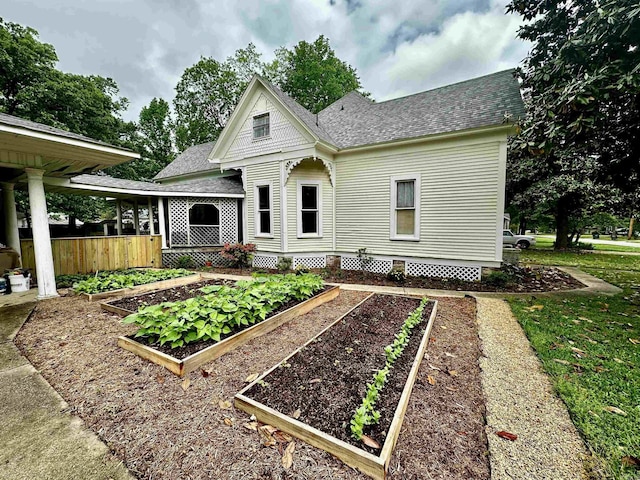 rear view of property with a vegetable garden, roof with shingles, and fence