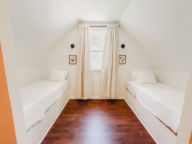 bedroom with dark wood-type flooring, a textured ceiling, and vaulted ceiling