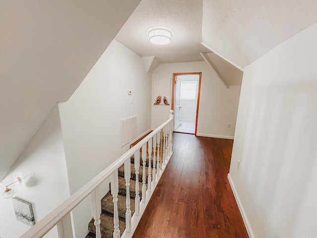 hallway featuring dark wood-type flooring, a textured ceiling, and lofted ceiling