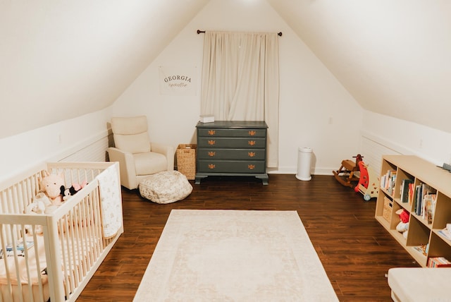 bedroom featuring dark hardwood / wood-style flooring, lofted ceiling, and a crib