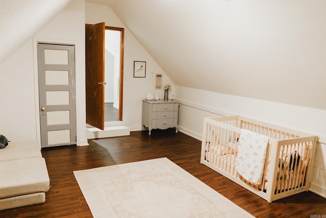 bedroom featuring a nursery area, dark wood-type flooring, and lofted ceiling