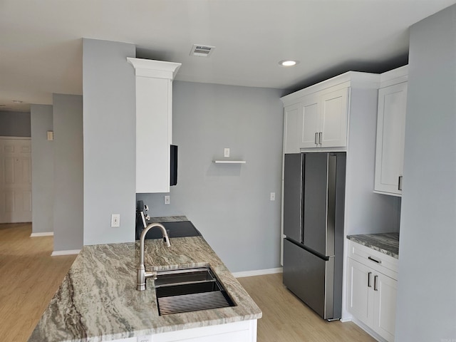 kitchen featuring light stone counters, white cabinetry, stainless steel refrigerator, sink, and light hardwood / wood-style flooring