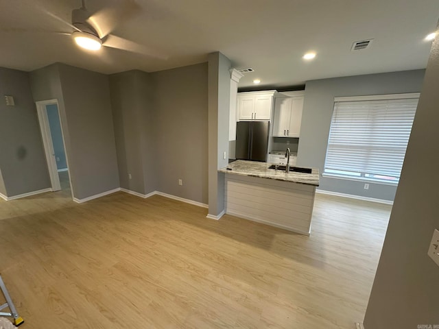 kitchen featuring sink, light stone countertops, white cabinetry, light hardwood / wood-style flooring, and stainless steel fridge