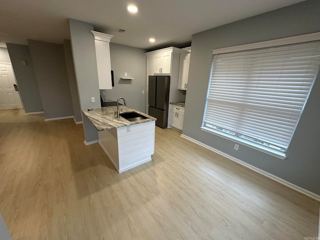 kitchen featuring black refrigerator, white cabinets, kitchen peninsula, sink, and light wood-type flooring