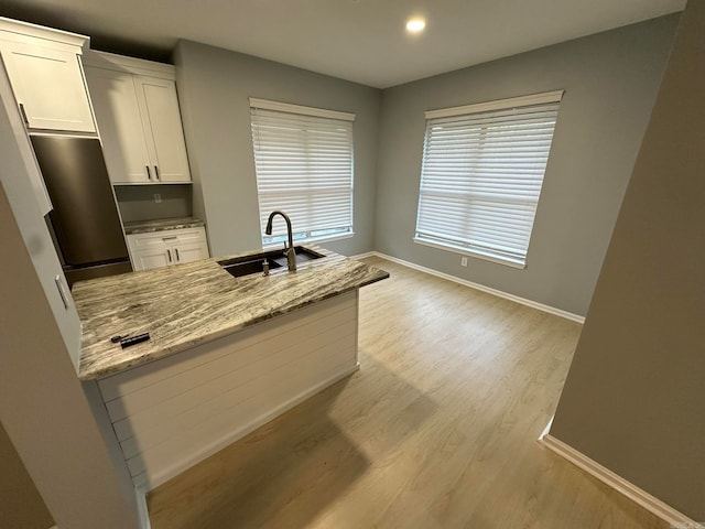 kitchen with light hardwood / wood-style floors, light stone counters, white cabinets, sink, and stainless steel refrigerator