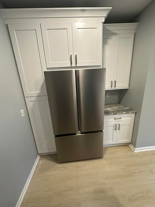 kitchen with white cabinetry, stainless steel refrigerator, light stone countertops, and light hardwood / wood-style flooring