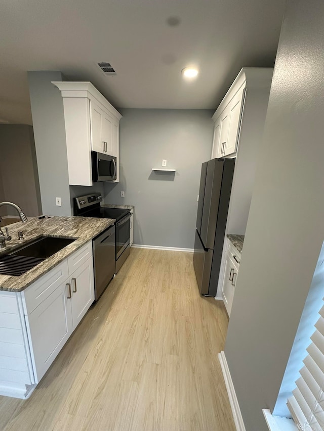 kitchen with sink, appliances with stainless steel finishes, light stone countertops, white cabinets, and light wood-type flooring