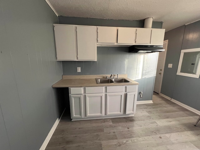 kitchen featuring white cabinets, a textured ceiling, sink, wooden walls, and light hardwood / wood-style flooring