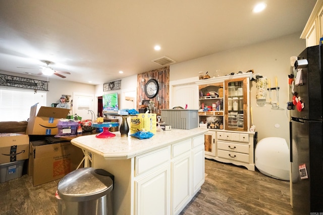 kitchen featuring dark hardwood / wood-style flooring, black fridge, ceiling fan, and a kitchen island with sink