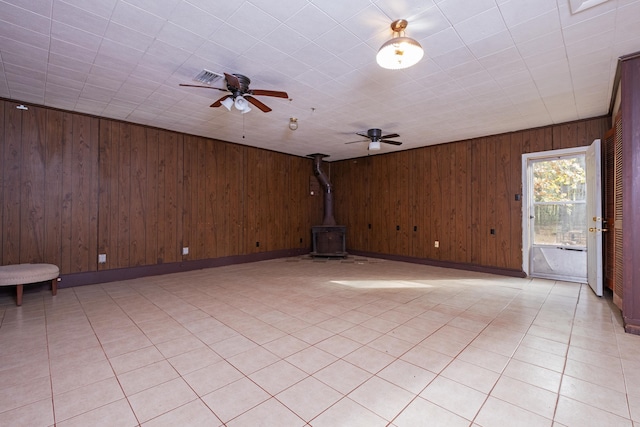 spare room with a wood stove, wood walls, and ceiling fan