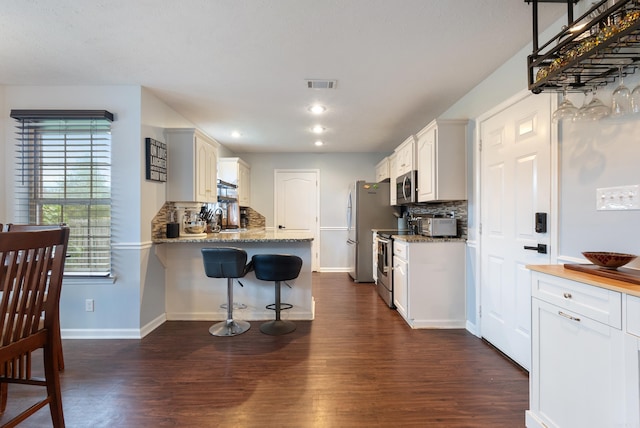 kitchen featuring dark hardwood / wood-style flooring, tasteful backsplash, appliances with stainless steel finishes, and white cabinets