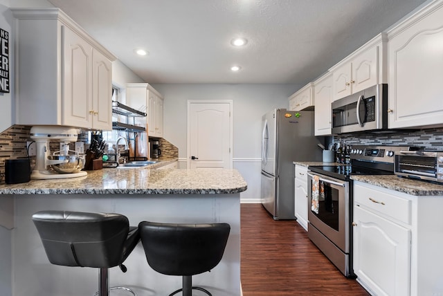 kitchen with appliances with stainless steel finishes, sink, white cabinets, dark wood-type flooring, and kitchen peninsula