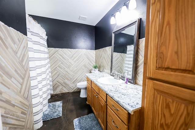 bathroom with toilet, vanity, and tile walls