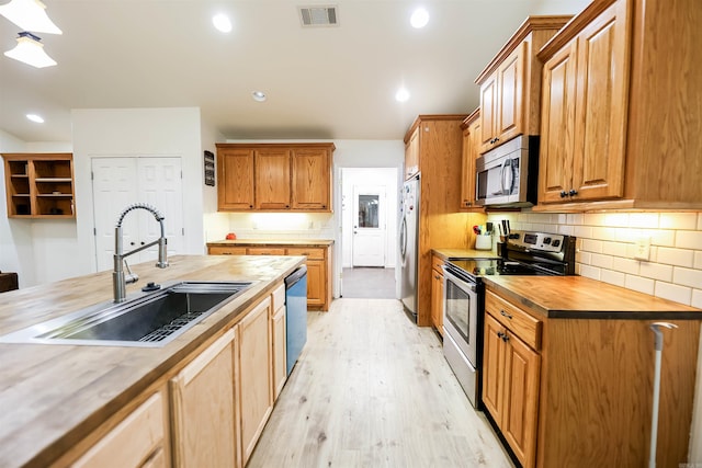 kitchen with butcher block counters, stainless steel appliances, sink, tasteful backsplash, and light hardwood / wood-style flooring