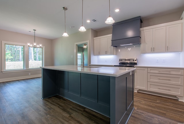 kitchen featuring decorative light fixtures, white cabinetry, premium range hood, and an island with sink