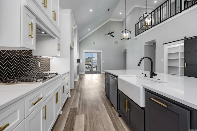 kitchen featuring white cabinets, a barn door, sink, high vaulted ceiling, and decorative light fixtures