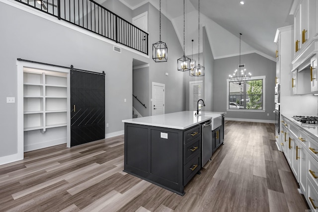 kitchen with white cabinets, a center island with sink, a barn door, and crown molding