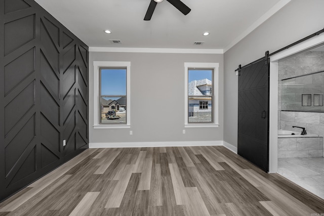 interior space featuring crown molding, light wood-type flooring, a barn door, and ceiling fan