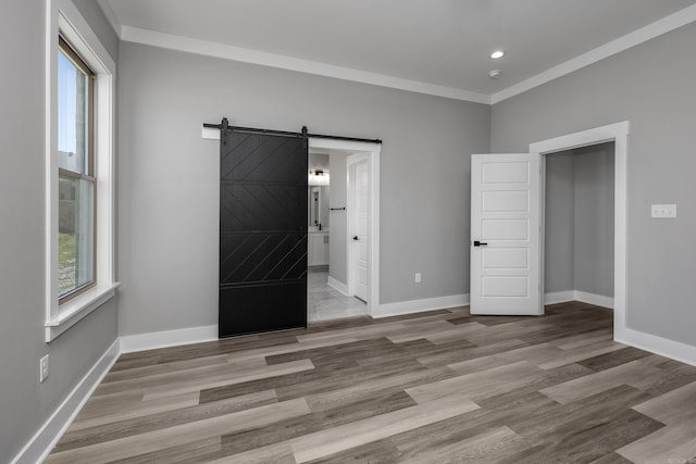 unfurnished bedroom with a barn door, connected bathroom, light wood-type flooring, and ornamental molding