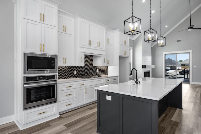 kitchen featuring light hardwood / wood-style floors, an island with sink, white cabinetry, appliances with stainless steel finishes, and decorative light fixtures