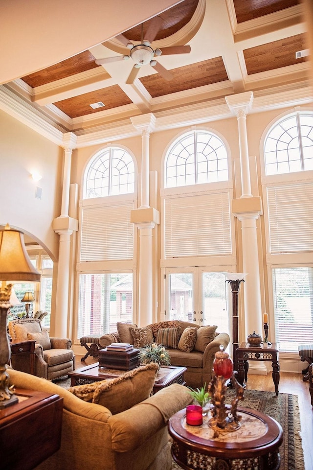 living room featuring crown molding, a towering ceiling, coffered ceiling, hardwood / wood-style flooring, and decorative columns