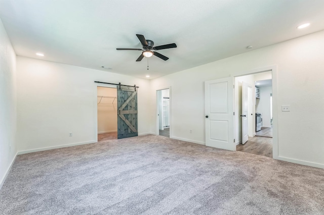 unfurnished bedroom with a closet, a walk in closet, a barn door, light colored carpet, and ceiling fan