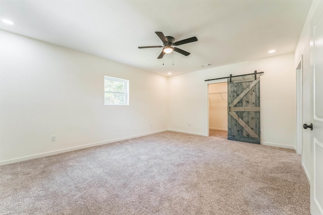 carpeted empty room with a barn door and ceiling fan