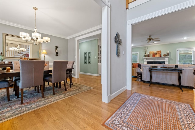 dining space with ceiling fan with notable chandelier, wood-type flooring, a tile fireplace, and crown molding