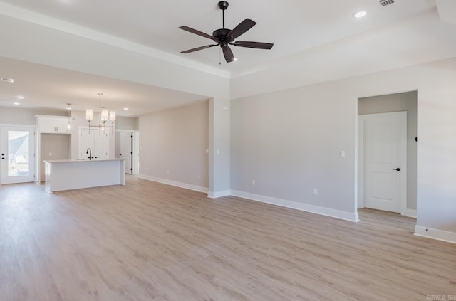 unfurnished living room with ceiling fan with notable chandelier, sink, and light hardwood / wood-style flooring