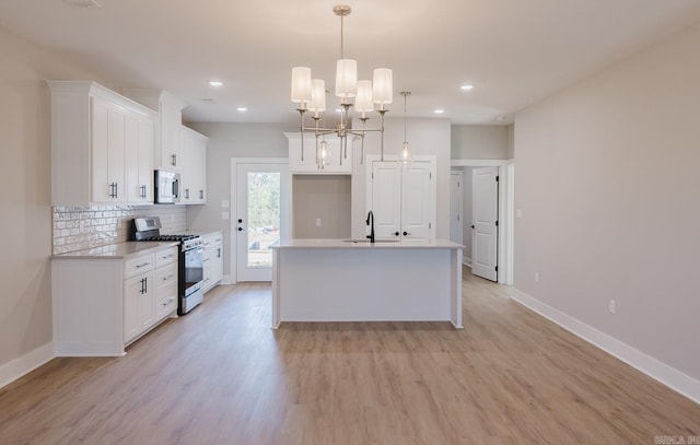 kitchen with stainless steel appliances, white cabinetry, a center island with sink, decorative light fixtures, and light hardwood / wood-style flooring