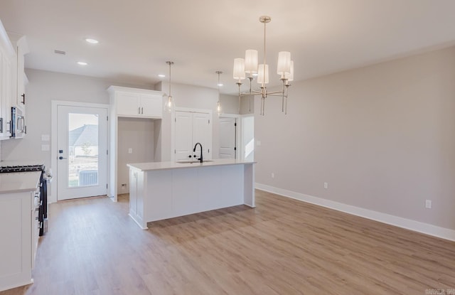 kitchen with a center island with sink, pendant lighting, sink, gas stove, and white cabinetry