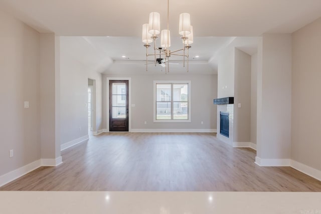 unfurnished living room with a brick fireplace, light hardwood / wood-style floors, and a notable chandelier