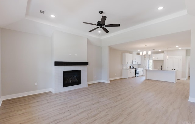 unfurnished living room featuring ceiling fan with notable chandelier, light hardwood / wood-style floors, sink, and a raised ceiling