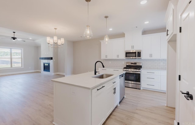 kitchen featuring sink, a kitchen island with sink, white cabinetry, appliances with stainless steel finishes, and decorative light fixtures