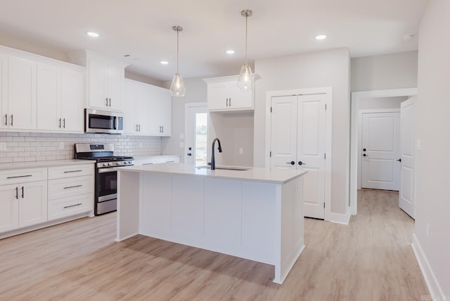 kitchen with a center island with sink, appliances with stainless steel finishes, sink, white cabinets, and light hardwood / wood-style flooring