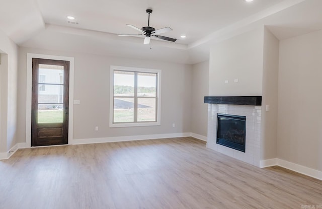 unfurnished living room with a fireplace, ceiling fan, light hardwood / wood-style floors, and a raised ceiling